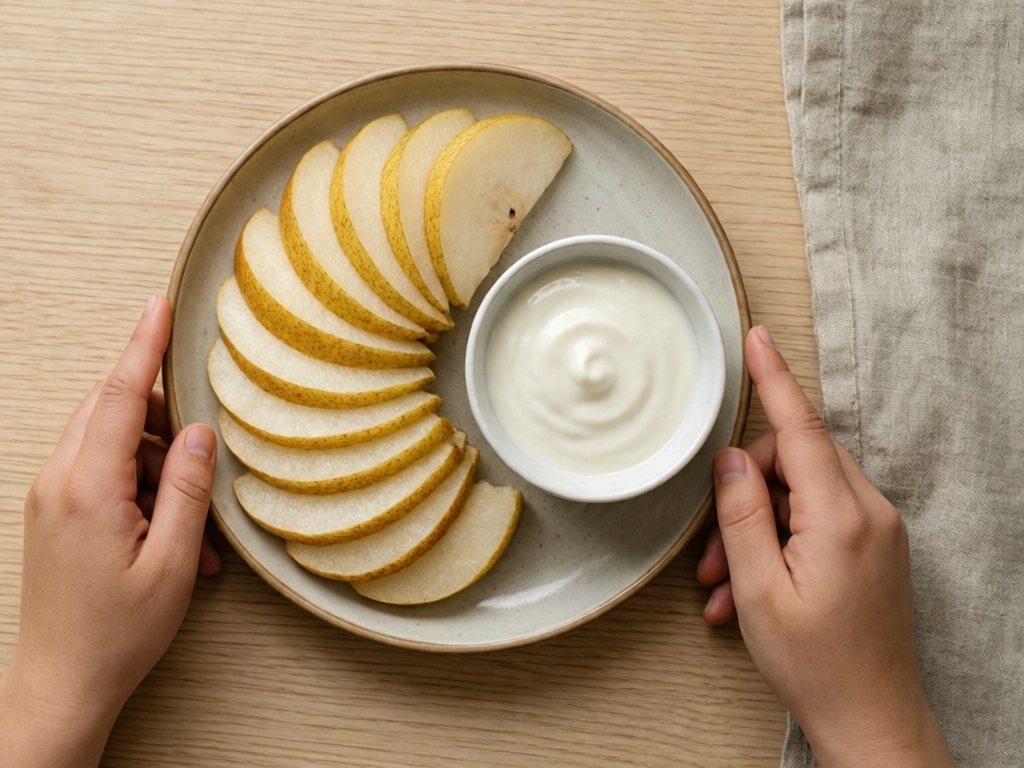 Thin pear slices fanned on a plate beside a small dish of plain yogurt for dipping
